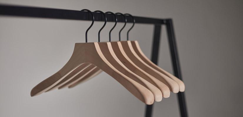 Hangers of London Five wooden hangers hanging on a black metal clothes rail, with a plain grey background.