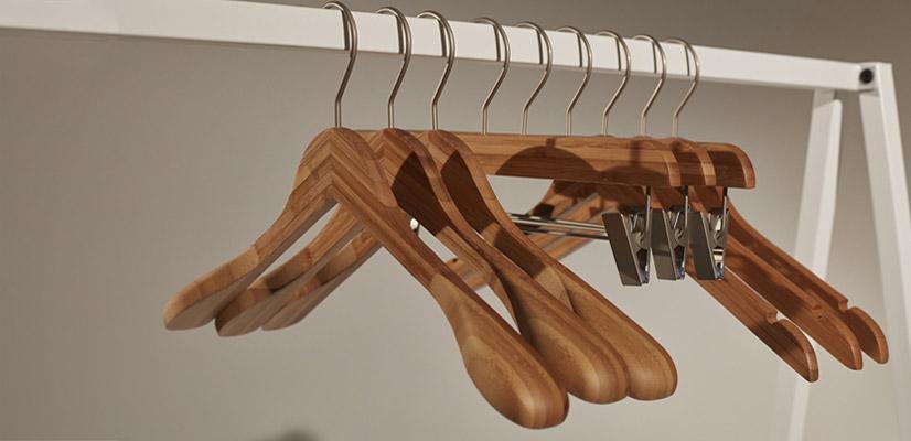 Hangers of London Seven wooden clothes hangers and one wooden hanger with metal clips hang on a white metal clothes rail against a plain background.