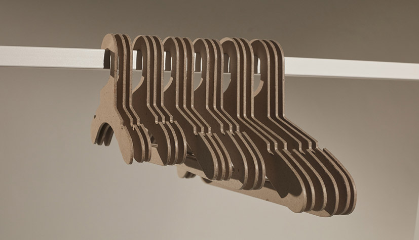 Hangers of London A row of sustainable brown cardboard hangers is neatly arranged on a white rod. The background is a plain gradient of neutral beige tones.