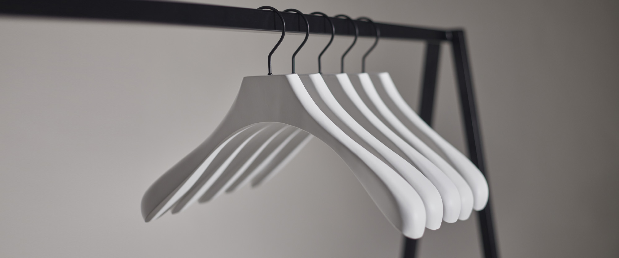 Hangers of London Six white wooden hangers hang neatly on a black metal clothes rail against a plain, neutral background.