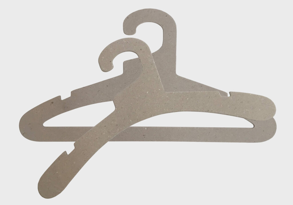 Hangers of London Two overlapping beige clothing hangers are displayed against a plain white background. The hangers have notches on the shoulders for securing garments with straps. The design is simple and functional, suitable for organizing clothes in a closet.