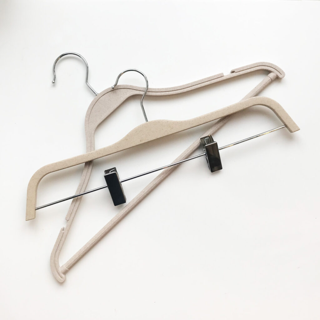 Hangers of London Two beige clothing hangers are placed against a white background. One hanger is a standard design with a curved hook, and the other has clips on a metal bar for holding pants or skirts. The hangers are slightly overlapped.