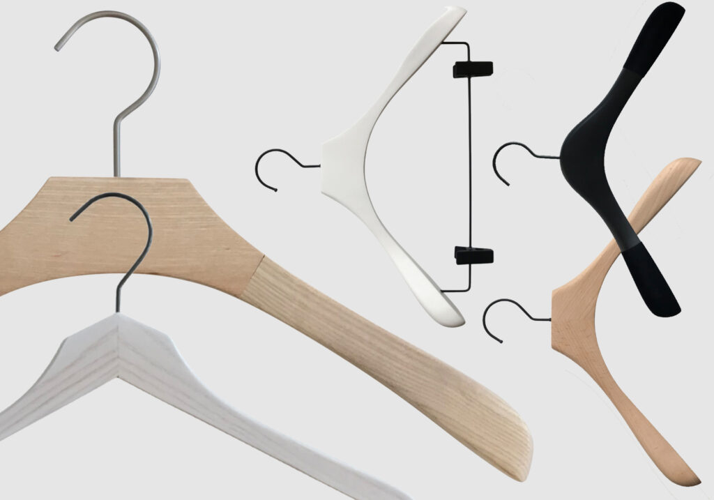 Hangers of London An assortment of various coat hangers on a white background. The collection includes wooden and plastic hangers in different shapes and colors, such as natural wood, white, black, and a clip hanger with a white and black combination.