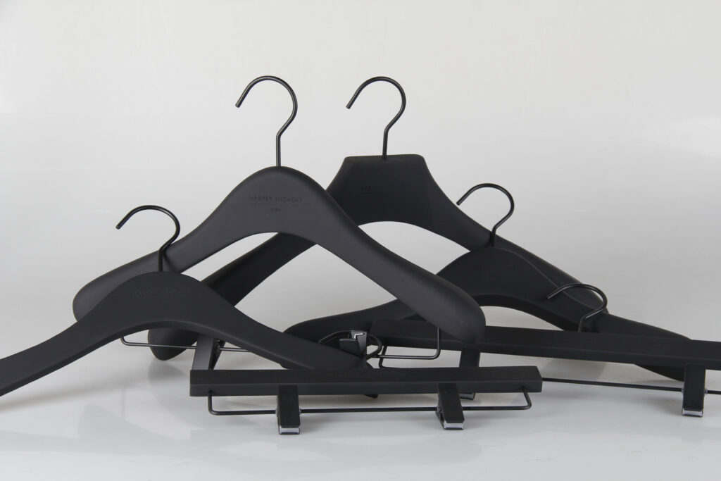 Hangers of London A group of black clothes hangers, including standard and clip hangers, is arranged against a white background. The hangers vary in design, with some featuring flat shoulders and curved hooks, while others have clips for hanging trousers or skirts.